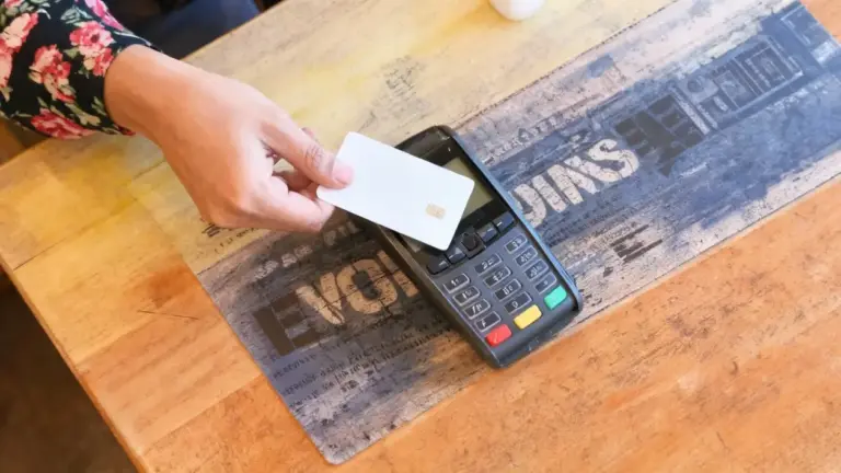 Una mano avvicina una carta di pagamento a un terminale POS su un tavolo di legno