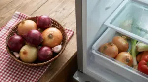 Cestino con cipolle e spicchi d’aglio accanto al cassetto del frigorifero con cipolle e verdure