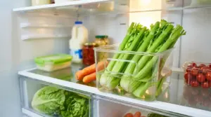 Sedano fresco conservato in un contenitore con acqua nel frigorifero, accanto ad altre verdure