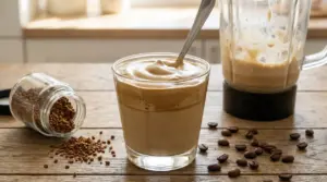 Bicchiere di crema al caffè con cucchiaio, vicino a frullatore e caffè solubile su tavolo di legno