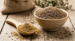 Ciotola di semi di cumino e cucchiaio con cumino in polvere su un tavolo di legno rustico