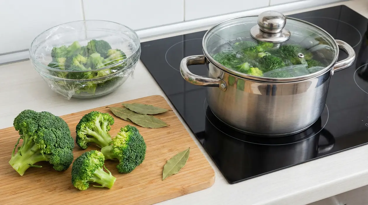Broccoli freschi su tagliere e in pentola in ebollizione su fornello a induzione