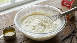 Ciotola di vetro con crema chantilly montata a mano con una frusta su un tavolo di legno