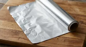 Rotolo di foglio di alluminio srotolato su un tagliere di legno, con superficie lucida visibile