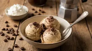 Ciotola con tre palline di gelato al caffè con chicchi e scaglie di cioccolato su tavolo di legno