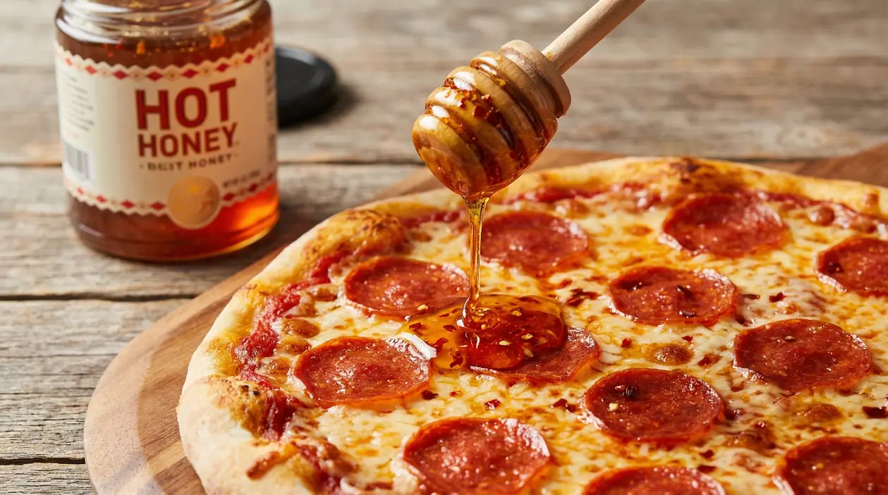 Hot honey colato con spargimiele su una pizza al salame, con barattolo di miele piccante sullo sfondo