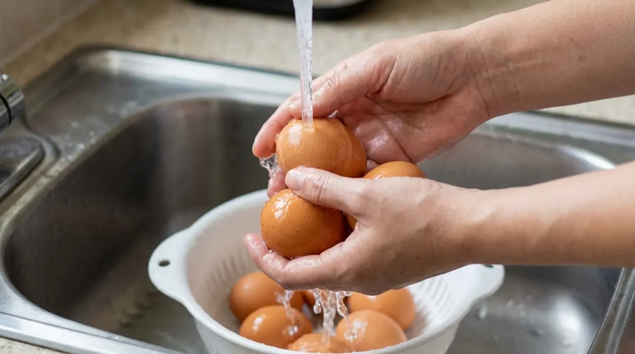 Mani che lavano uova sotto l’acqua corrente nel lavello della cucina