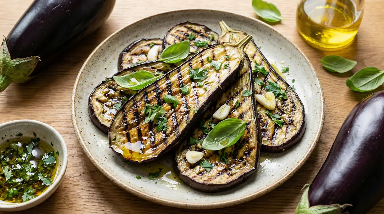 Fette di melanzane grigliate condite con erbe, aglio e olio su un piatto di ceramica