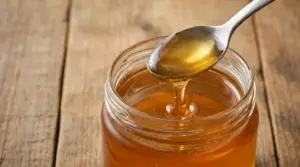 Cucchiaio di metallo con miele sopra un barattolo di miele appoggiato su un tavolo di legno