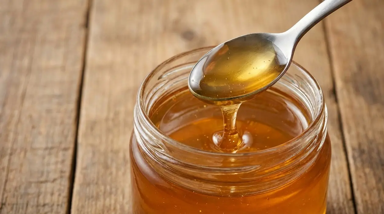 Cucchiaio di metallo con miele sopra un barattolo di miele appoggiato su un tavolo di legno