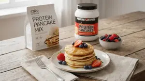 Pancake light con sciroppo e frutti di bosco su piatto, con mix proteico sul tavolo per colazione