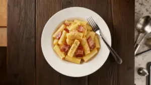 Piatto di pasta alla carbonara cremosa con guanciale e pepe nero su tavolo in legno