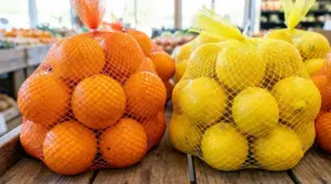 Sacchetti a rete arancione con arance e a rete gialla con limoni esposti su un banco di frutta al supermercato