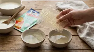 Fogli di gelatina alimentare in ammollo in ciotole d’acqua su tavolo di legno, con una mano che li solleva