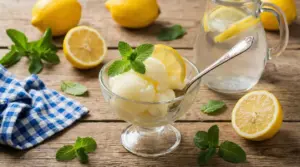 Coppa di sorbetto al limone con foglie di menta, accompagnata da limoni freschi su un tavolo rustico
