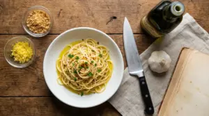 Piatto di spaghetti aglio, olio e peperoncino con ingredienti su un tavolo rustico