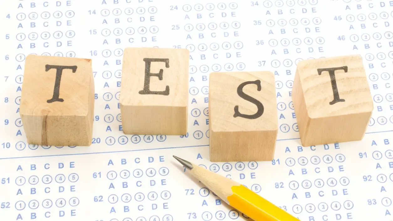 Matita su modulo di test a scelta multipla con blocchi di legno che formano la parola TEST