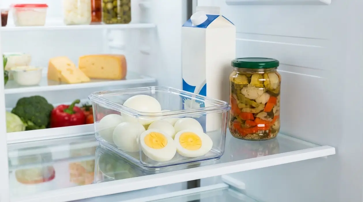 Uova sode in contenitore ermetico riposte in frigorifero su ripiano, con altri alimenti sullo sfondo